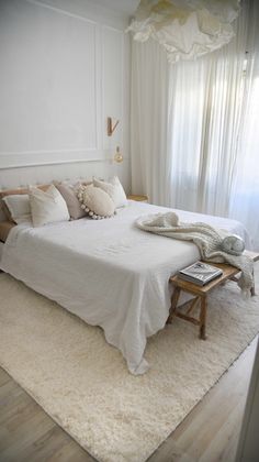 a white bed sitting on top of a wooden floor next to a window covered in curtains