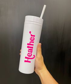 a hand holding a white tumbler cup with pink lettering on it that says hey