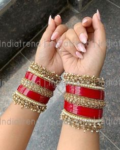 two hands holding onto each other with red and gold bracelets on their wristes