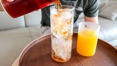 a person pouring orange juice into a glass on top of a wooden table next to another cup