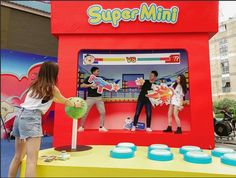 two girls are playing with a toy machine in front of a storefront sign that says supermint