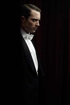 a man in a tuxedo looking out from behind a dark clothed curtain