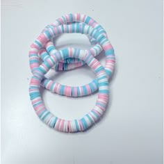 three pink and blue bracelets sitting on top of a white table next to each other