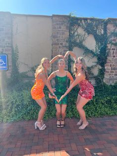 three young women are posing in front of a brick wall with ivy growing on it