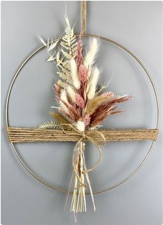 a metal circle hanging on the wall with some dried flowers in it and two feathers attached to it