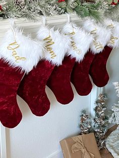 christmas stockings hanging from a mantel decorated with red and white furs, gold lettering