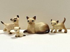 three small figurines of siamese cats on a white surface with one cat looking at the camera