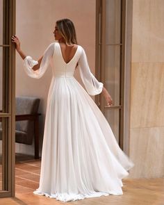 a woman in a white wedding dress is standing by an open door and looking into the room