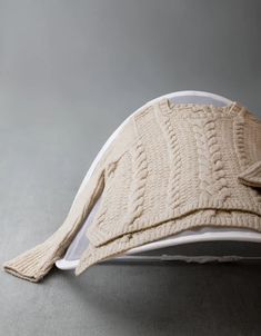 a white hat with a cabled design on the front and side, sitting on top of a gray surface