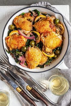 a white bowl filled with chicken and vegetables on top of a table next to utensils