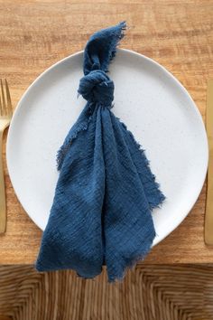 a white plate topped with a blue napkin next to gold fork and knife set on top of a wooden table