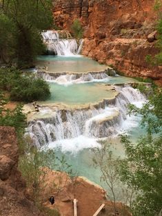 the water is blue and green as it flows through some rocks in front of a waterfall