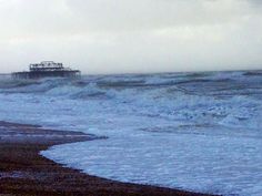 an ocean beach with waves crashing on the shore and a pier in the distance under a cloudy sky