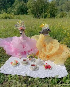 two dogs dressed up as princesses sitting on a blanket with tea cups in front of them