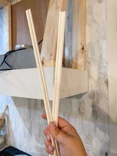 a person holding two chopsticks in front of a kitchen counter top with wooden cabinets