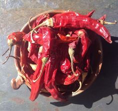 some red peppers are in a basket on the ground and one is still attached to it