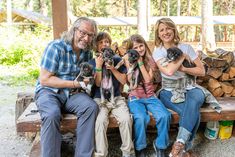 a group of people sitting on top of a wooden bench with dogs in their hands