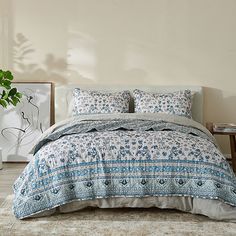 a bed with blue and white bedspread in a bedroom next to a plant