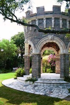 an arch in the middle of a garden with flowers growing on it and trees around