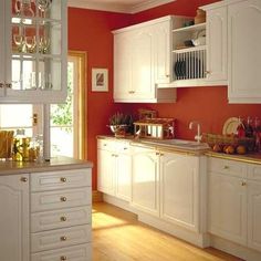 a kitchen with red walls and white cabinets is pictured in this image, there are wine glasses on the counter