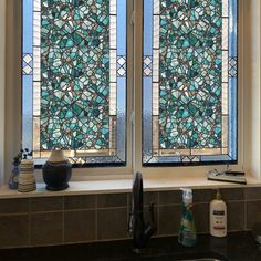 two stained glass windows in a kitchen next to a window sill with bottles on the counter