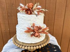 a three tiered white cake with orange flowers and feathers sitting on top of a table