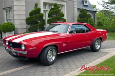 a red and white muscle car parked in front of a house