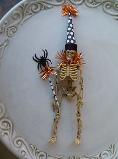 a skeleton in a witches hat is on a white plate with orange and black decorations