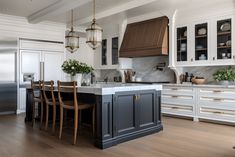 a large kitchen with white cabinets and wooden floors is pictured in this image, there are several chairs around the island