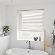 a white bath tub sitting under a window next to a towel rack and potted plant