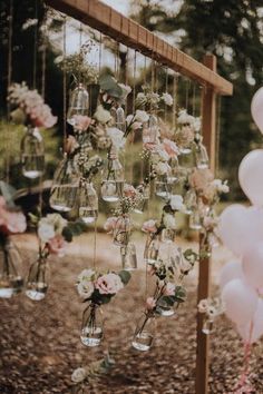 several vases filled with flowers and balloons hanging from a wooden trellis in the woods