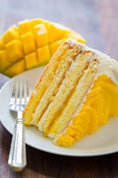 a piece of cake on a white plate next to a fork and mango wedges