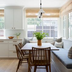 a kitchen filled with lots of white cabinets and wooden chairs next to a window seat