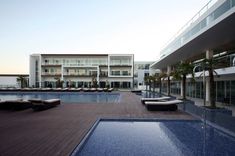 an empty swimming pool in front of a hotel with chaise lounges on the deck