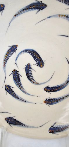 a white plate with blue and yellow fish on it's side, in the middle of a spiral design