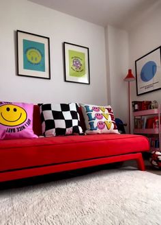 a red couch with pillows on it in front of two pictures and a bookcase