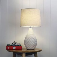 a white lamp sitting on top of a wooden table next to a red book and a pair of glasses