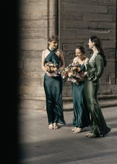 three women in long dresses standing next to each other and holding bouquets with flowers