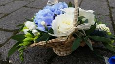 a basket filled with blue and white flowers on top of a stone floor next to a sidewalk