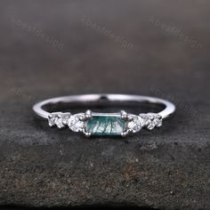 a white gold ring with an emerald stone and three diamonds on the side, sitting on top of a rock