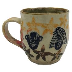 a coffee cup with two faces on the side and flowers painted on it's sides