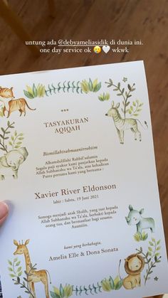 a person holding up a wedding card with animals on it and leaves in the background