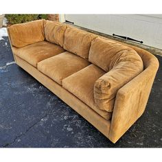 a brown couch sitting on top of a parking lot next to a garage door,