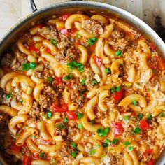 a large pot filled with pasta and meat on top of a wooden table next to green onions