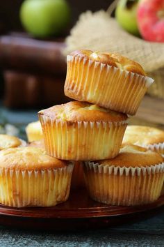 several muffins stacked on top of each other on a wooden plate next to an apple