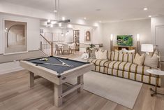 a living room filled with furniture and a pool table in front of a couch on top of a hard wood floor