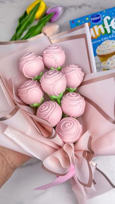 a hand holding a bouquet of pink cupcakes