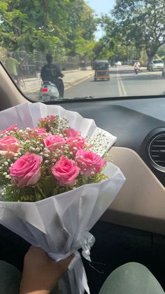 a bouquet of pink roses is sitting in the passenger seat of a car, while someone drives by