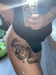 a woman with a dragon tattoo on her thigh holding a cell phone in her hand