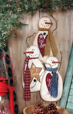 three snowmen are hanging on the side of a wooden fence with pine cones in front of them